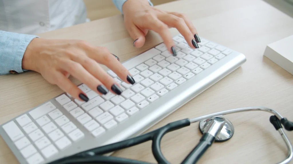 Typing on a keyboard beside a stethoscope